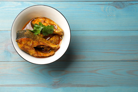 Tasty fish curry on light blue wooden table, top view. Space for text. Indian cuisine