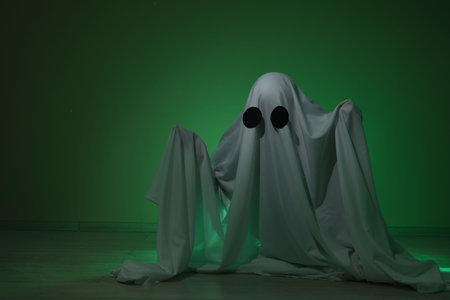 Creepy ghost. Woman covered with sheet in green light, space for textの写真素材