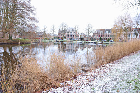 Picturesque view of water canal with moored boats, trees and buildings in city on winter dayの写真素材