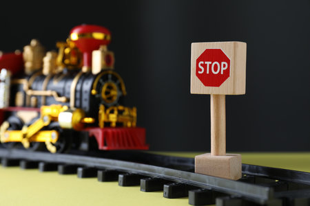 Road Stop sign as barrier blocking way for toy train on yellow surface, space for text. Development through obstacles overcomingの写真素材
