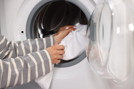 Woman putting laundry into washing machine indoors, closeupの写真素材