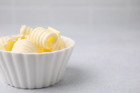 Tasty butter curls in bowl on light gray table, closeup. Space for textの写真素材