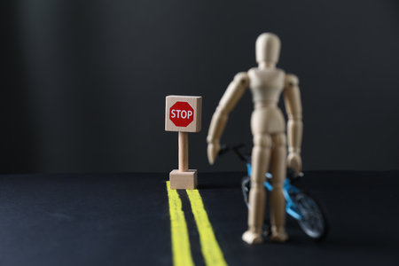 Development through barriers overcoming. Road Stop sign blocking way for wooden human figure with toy bicycle, space for textの写真素材