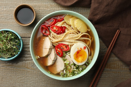 Delicious ramen in bowl, soy sauce and microgreens on wooden table, flat lay. Noodle soupの写真素材
