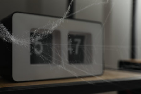 Cobweb near alarm clock on rack indoors, closeup