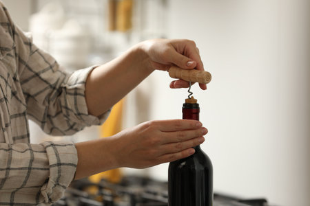 Woman opening wine bottle with corkscrew indoors, closeupの写真素材