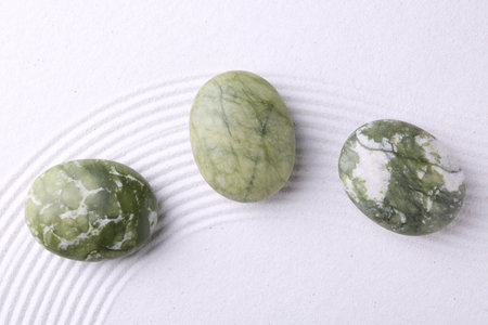 Zen garden stones on white sand with pattern, flat lay