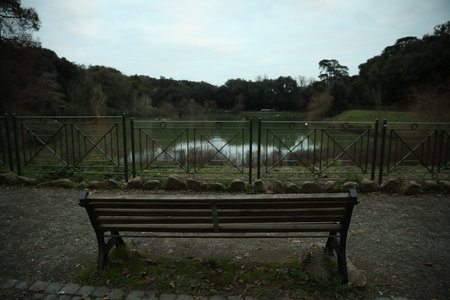Beautiful view of bench near lake in park on cloudy dayの写真素材