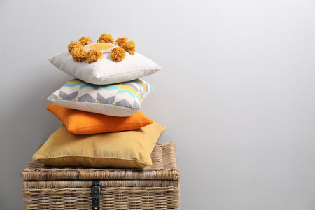 Soft pillows on wooden trunk near light gray wall, space for text