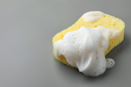 Yellow sponge with foam on gray background, closeup. Space for textの写真素材