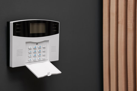 Home security alarm system on brown wall indoors, space for text