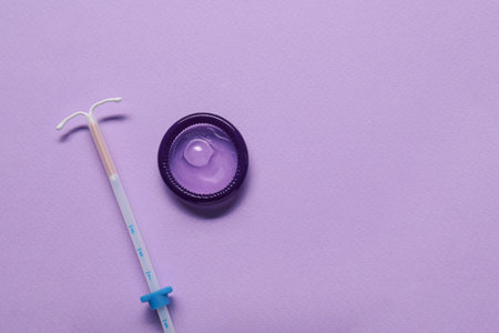 Condom and intrauterine device on lilac background, flat lay and space for text. Choosing method of...