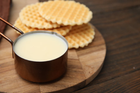 Tasty condensed milk and waffles on wooden table, closeup. Space for textの写真素材