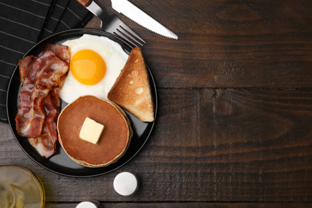 Tasty pancakes served with fried egg and bacon on wooden table, flat lay. Space for textの写真素材