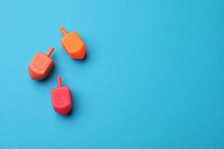 Colorful dreidels on light blue background, flat lay with space for text. Traditional Hanukkah game