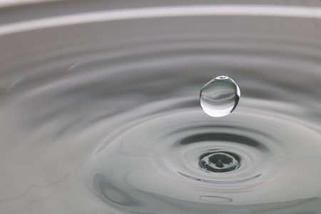 Drop falling into clear water on light gray background, closeup. Space for text
