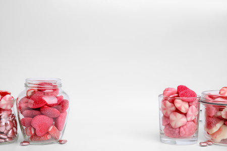 Different yummy pink candies in glass jars and bowls on white background, space for text
