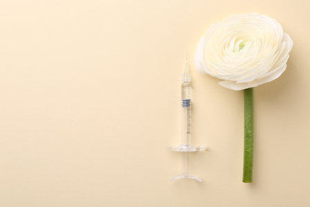 Cosmetology. Medical syringe and ranunculus flower on yellow background, flat lay. Space for textの写真素材