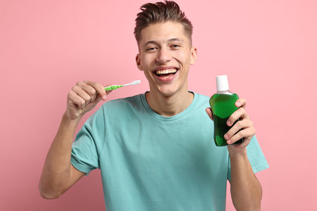 Young man with mouthwash and toothbrush on pink backgroundの写真素材