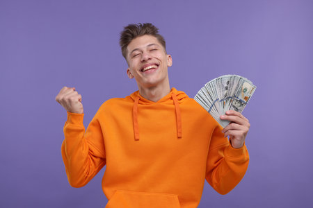 Happy man with money on purple backgroundの写真素材