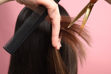 Hairdresser cutting client's hair with scissors on pink background, closeupの写真素材