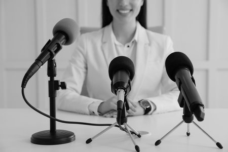 Journalist conference. Businesswoman giving interview at table with microphones indoors, closeup. Black and white effectの写真素材