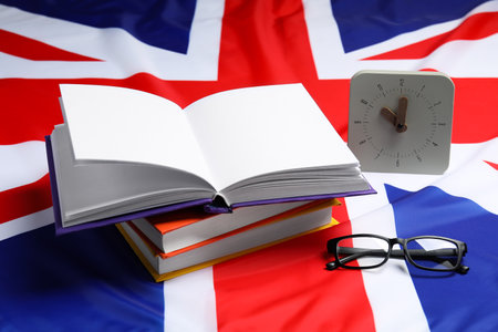 Learning foreign language. Different books, alarm clock and glasses on flag of United Kingdomの写真素材