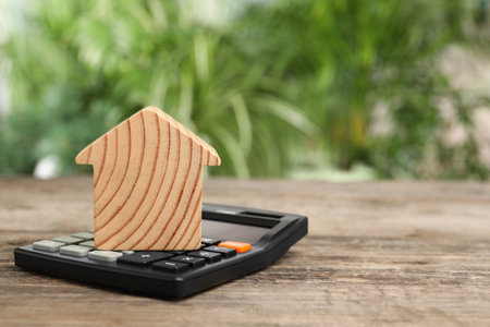 Mortgage concept. Model house and calculator on wooden table against blurred green background, space for textの写真素材