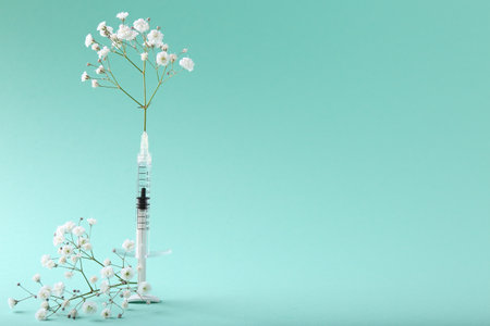 Cosmetology. Medical syringe and gypsophila flowers on turquoise background, space for textの写真素材