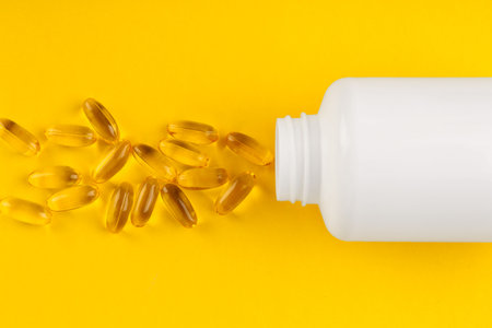 White medical bottle and vitamin capsules on yellow background, top viewの写真素材