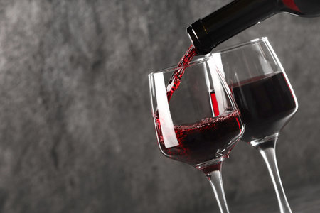 Pouring red wine into glass against gray background, closeup. Space for textの写真素材