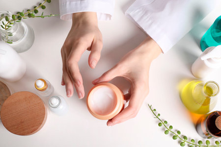 Dermatologist with jar of cosmetic product at white table, top view. Development and testingの写真素材