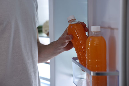 Man taking bottle of juice out of refrigerator at night, closeupの写真素材