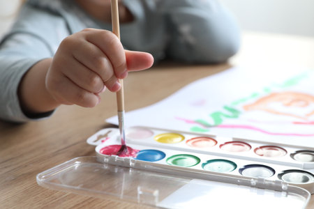 Little girl with brush drawing at wooden table indoors, selective focus. Child`s artの写真素材