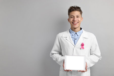 Mammologist with pink ribbon showing tablet on light gray background, space for text. Breast cancer awarenessの写真素材