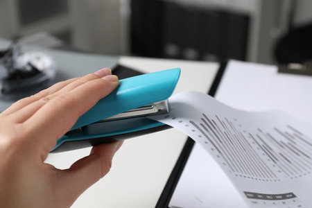 Woman with documents using stapler at white table indoors, closeupの写真素材