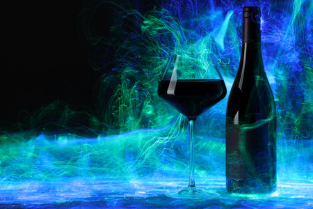 Red wine in glass and bottle in color lights on black background, space for textの写真素材