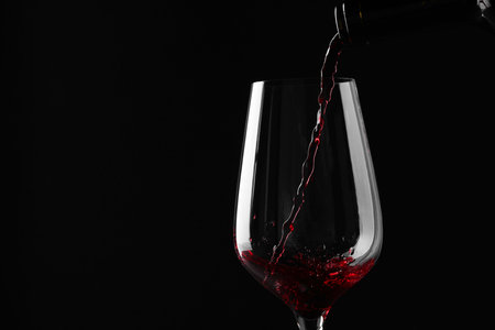Pouring red wine into glass against black background, closeup. Space for textの写真素材