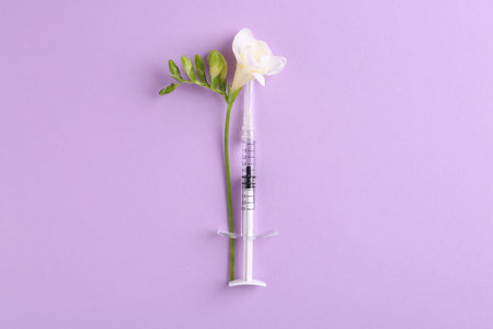 Cosmetology. Medical syringe and freesia flower on violet background, top viewの写真素材