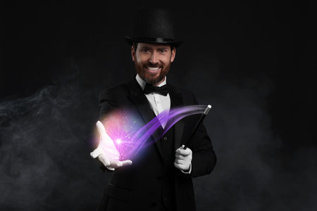 Magic and sorcery. Magician with wand and fantastic light in smoke on dark backgroundの写真素材
