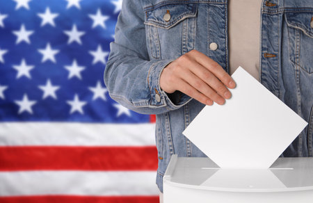 Election in USA. Man putting his vote into ballot box against national flag of United States,...