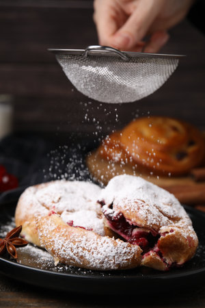 Woman dusting delicious buns with sugar powder at table, closeupの写真素材