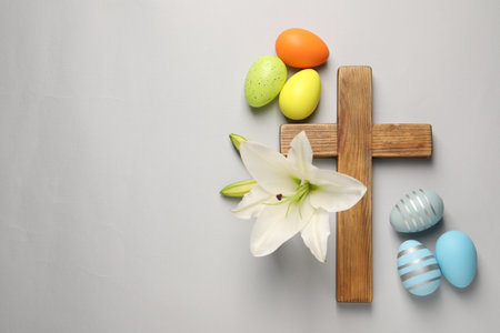 Wooden cross, painted Easter eggs and lily flowers on gray background, flat lay. Space for textの写真素材