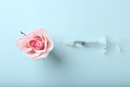 Cosmetology. Medical syringe and rose flower on light blue background, flat layの写真素材