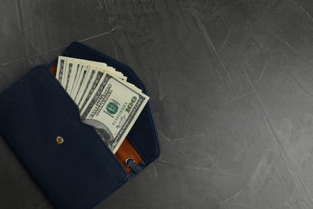 Money exchange. Wallet with dollar banknotes on dark gray textured background, top view. Space for textの写真素材
