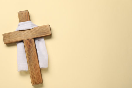 Wooden cross and white cloth on beige background, top view with space for text. Easter attributesの写真素材