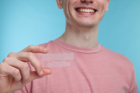 Young man with whitening strips on light blue background, closeupの写真素材