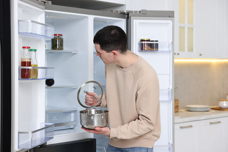 Man with pot near empty refrigerator in kitchenの写真素材