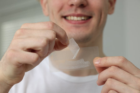 Young man with whitening strips indoors, closeup