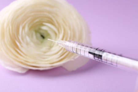 Cosmetology. Medical syringe and ranunculus flower on violet background, closeupの写真素材